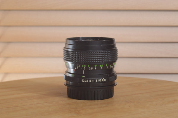 Vivitar Zoom PK Pentax 28-50mm f3.5-4.5 camera lens displayed on a surface with focus on lens details and markings